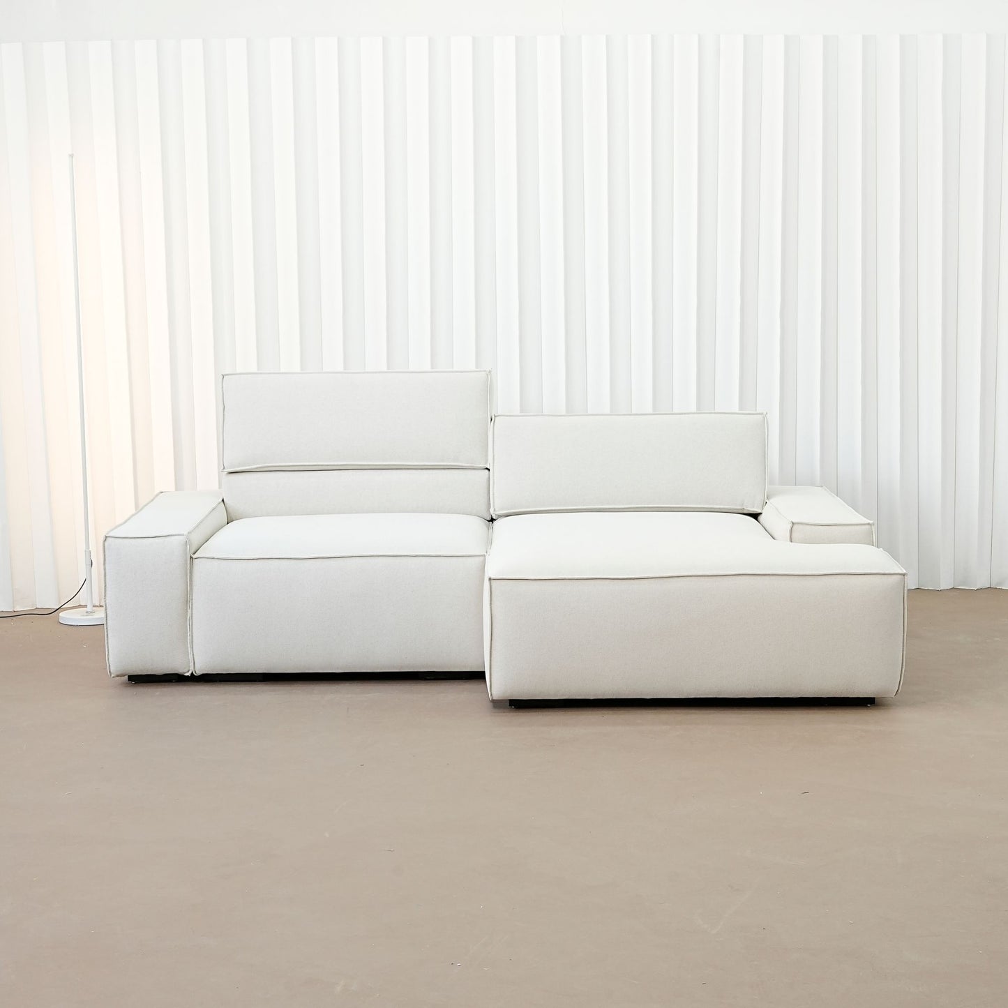Beige sectional sofa in a minimalistic room with white walls and a brown floor.