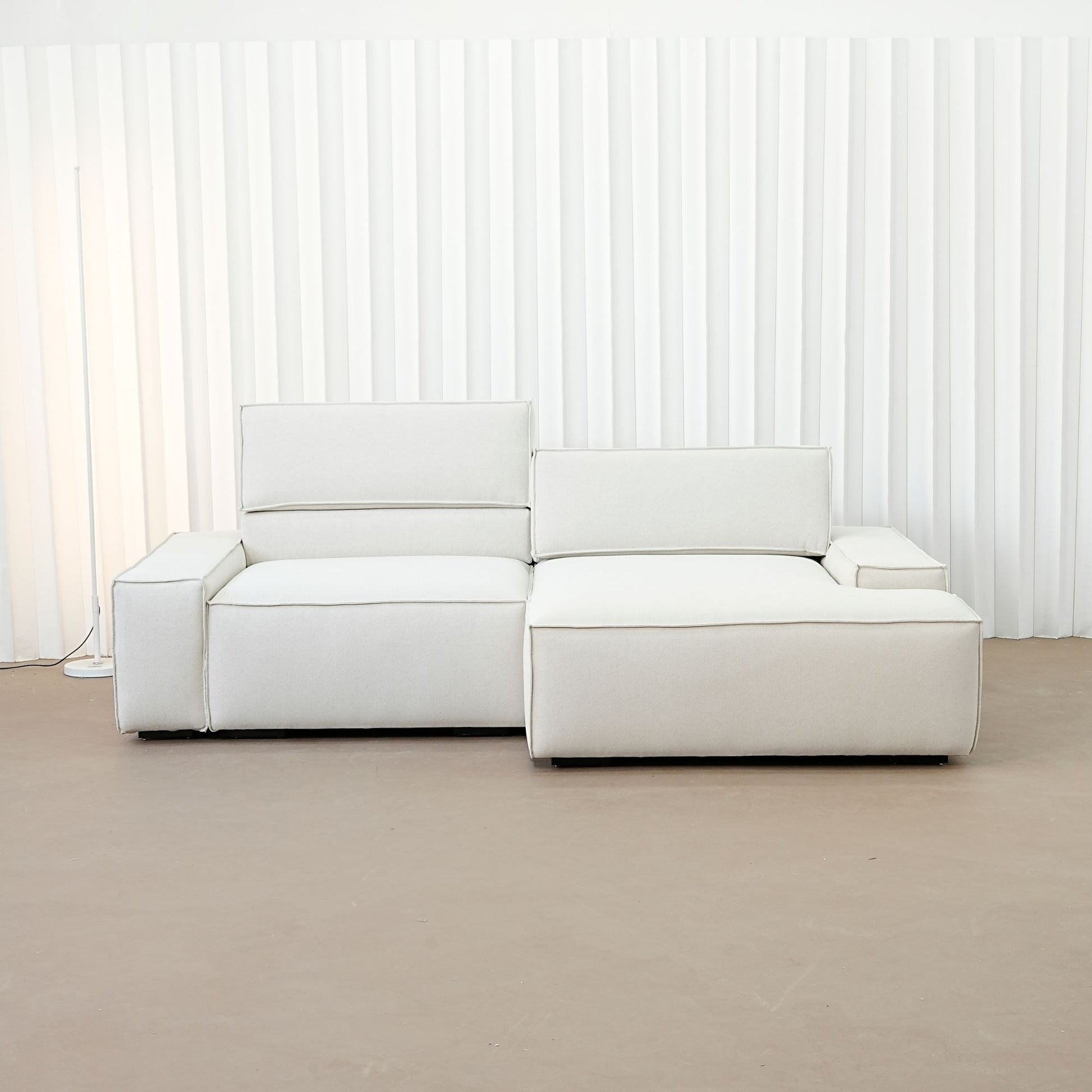 Beige sectional sofa in a minimalistic room with white walls and a brown floor.