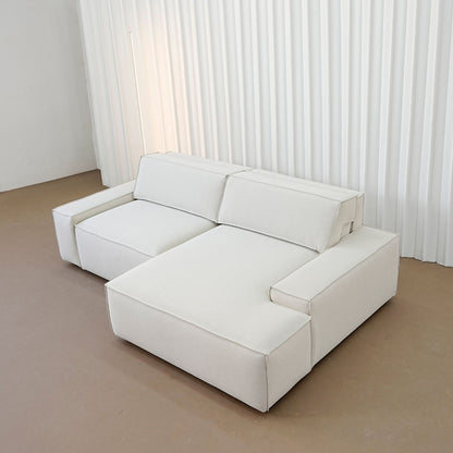 White sectional sofa in a minimalistic room with white curtains.
