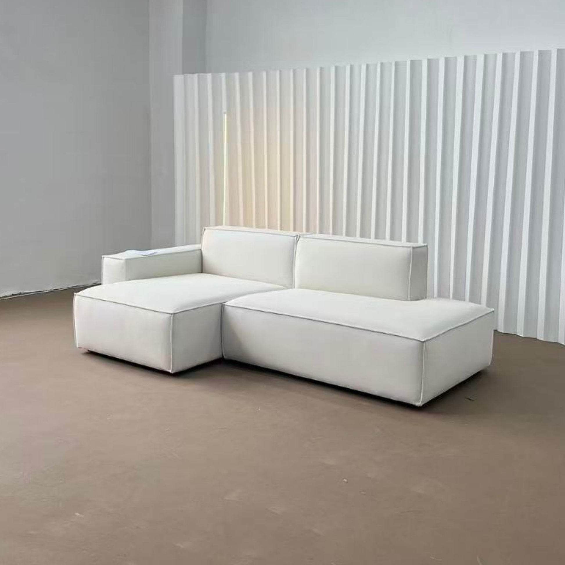 White sectional sofa in a minimalistic room with a striped wall.