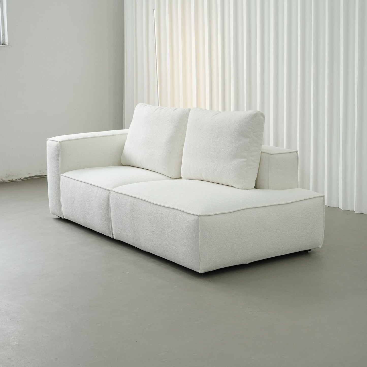 White sofa in a minimalistic room with light gray floor and white curtains.