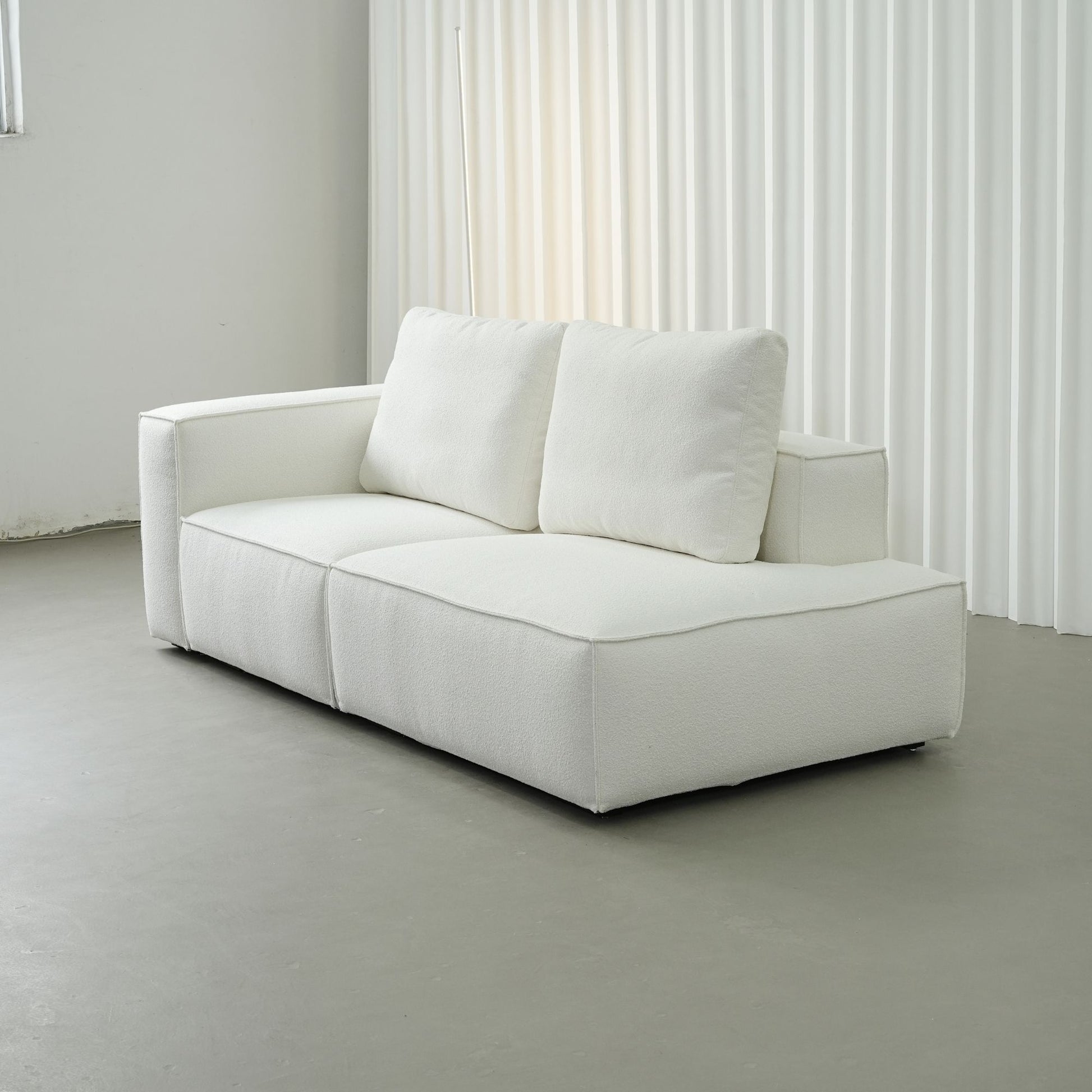 White sofa in a minimalistic room with light gray floor and white curtains.