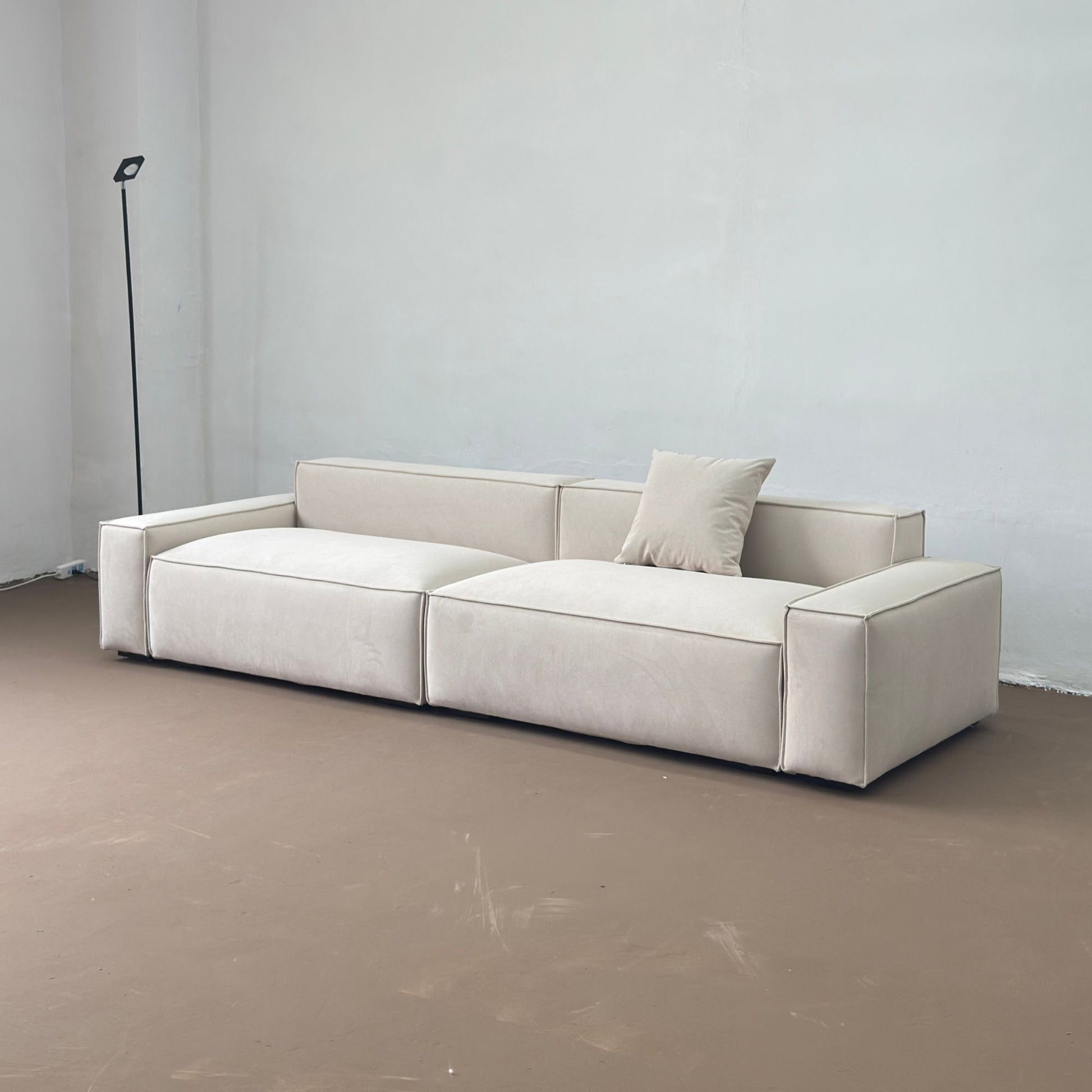 Beige sectional sofa in a minimalistic room with a plain wall and floor.