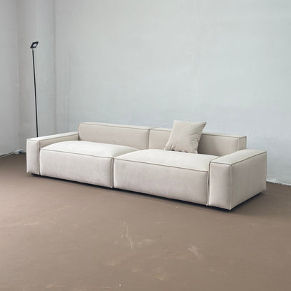 Beige sectional sofa in a minimalistic room with a plain wall and floor.
