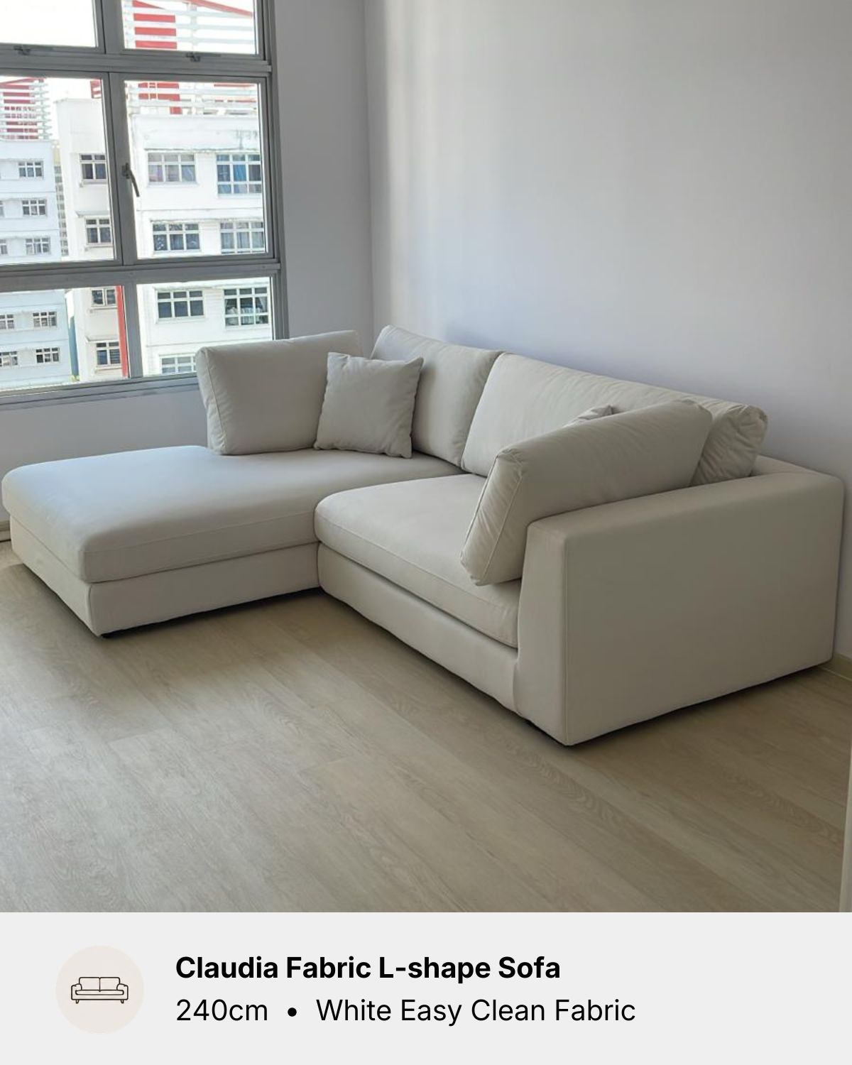 An L-shaped sectional sofa upholstered in white easy clean fabric, shown in a minimalist room with light wood floors and a large window.