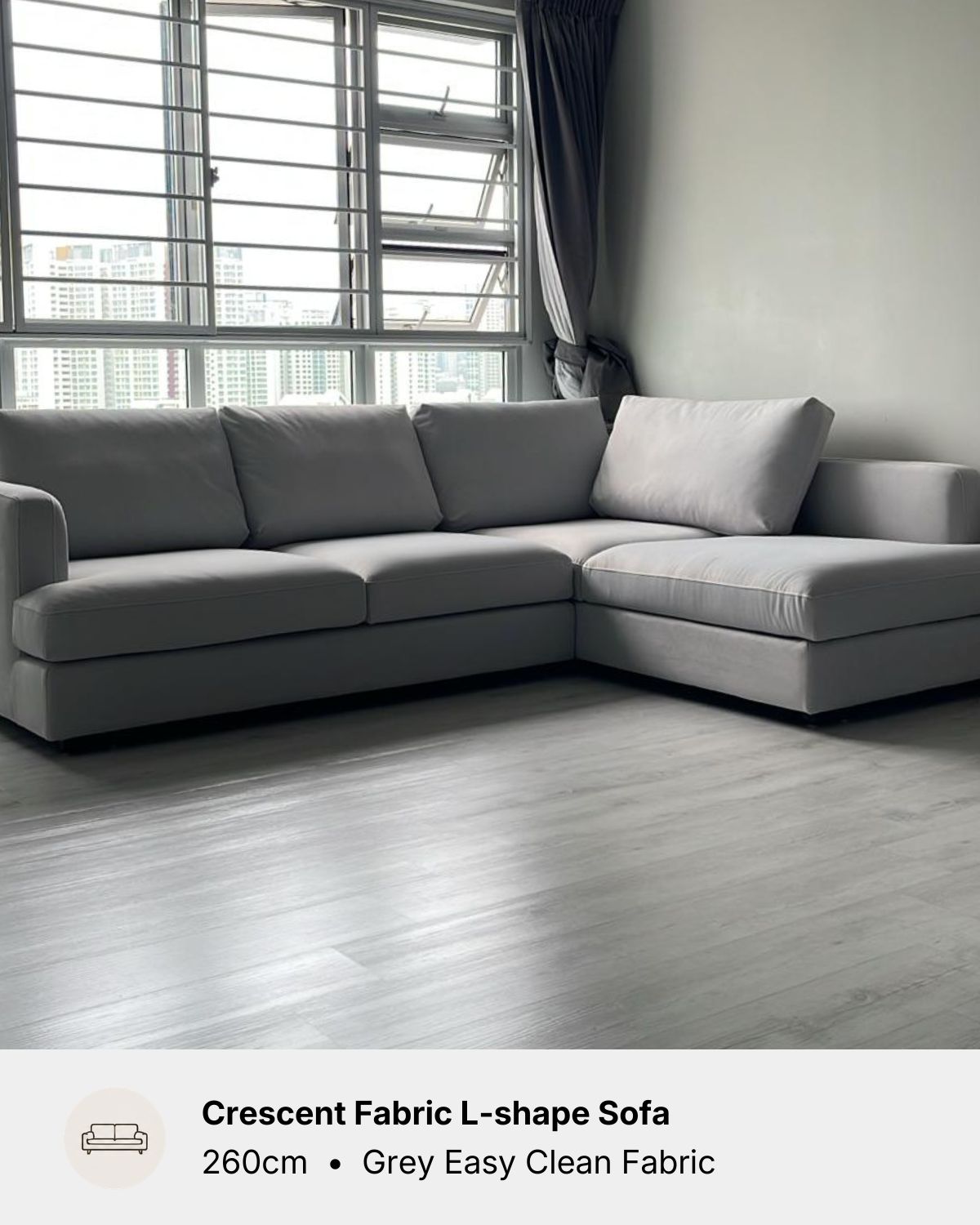 An L-shaped grey fabric sofa in a modern living room setting with grey wood flooring and a large window in the background. A text overlay at the bottom reads 'Crescent Fabric L-shape Sofa 260cm • Grey Easy Clean Fabric'.