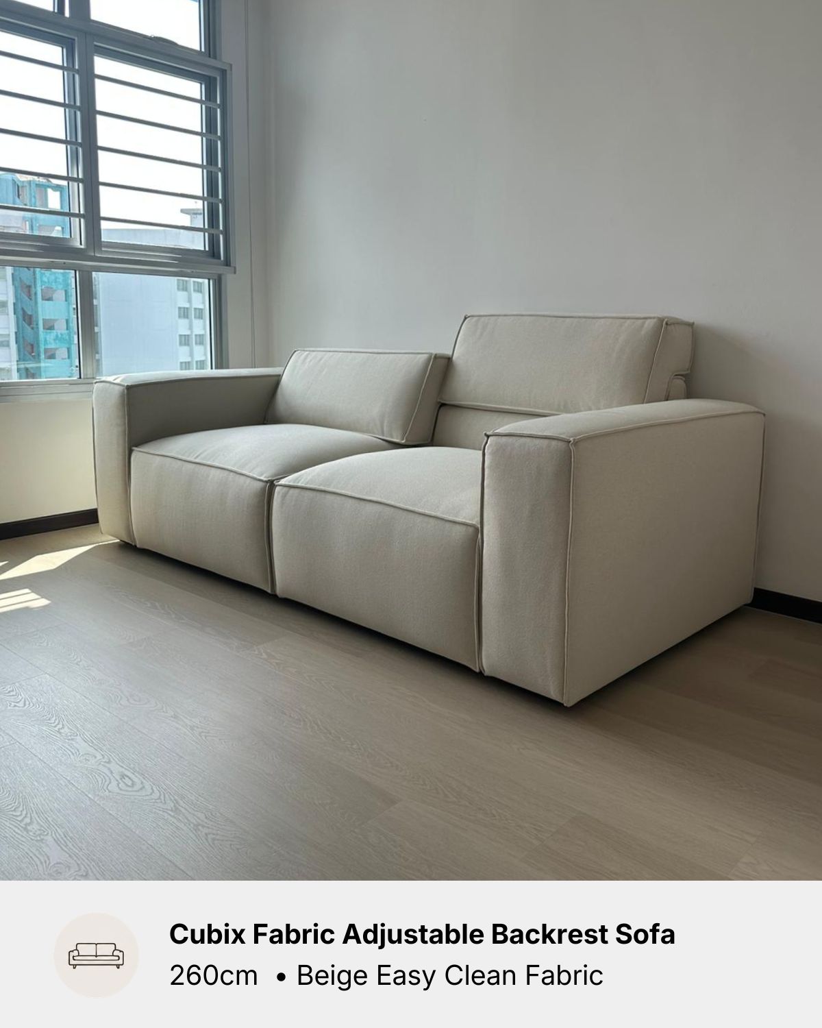 A beige fabric cubix sofa with adjustable backrests, shown in a minimalist room with light wood flooring and a window.