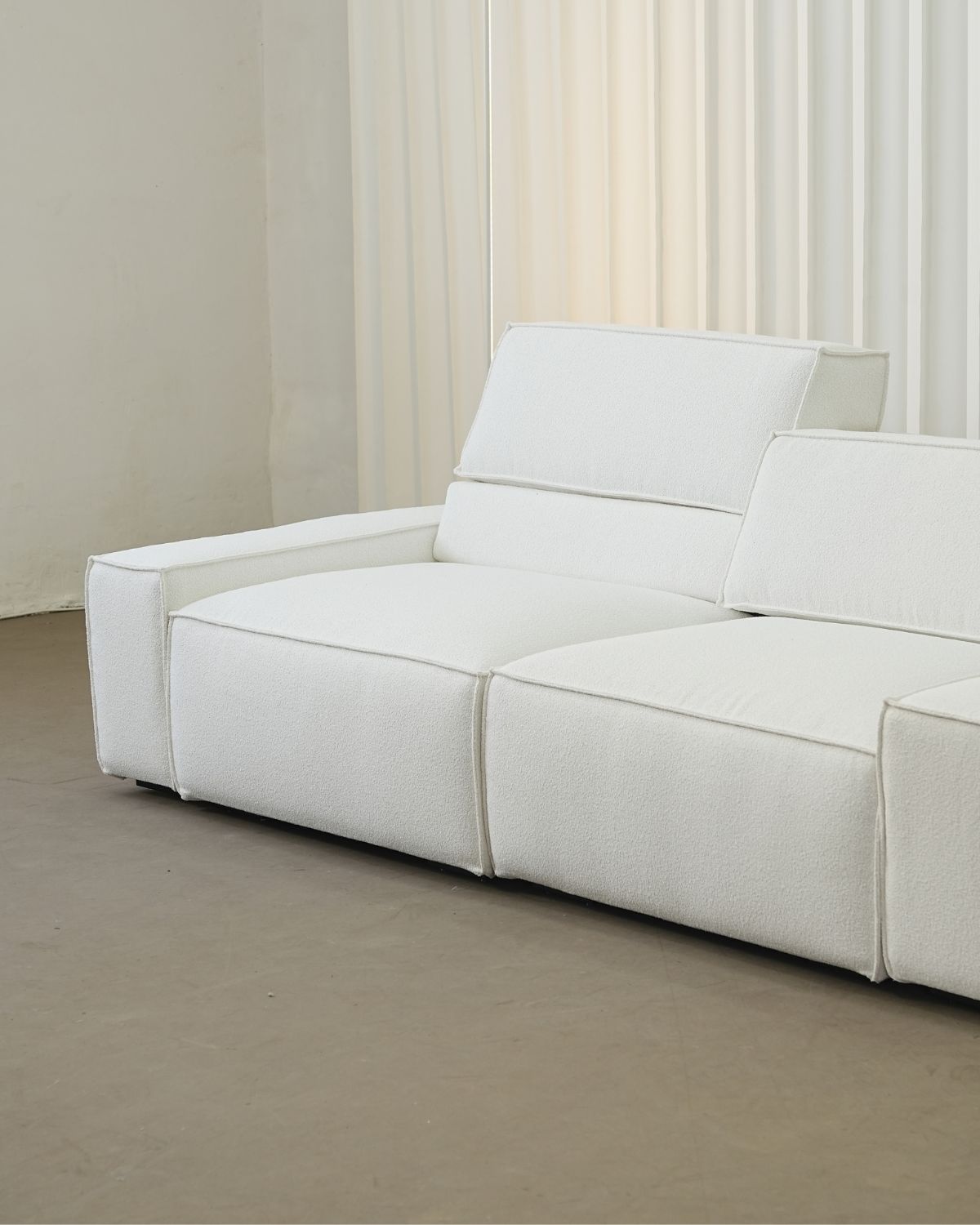 White high back sofa in a minimalistic room with neutral walls and flooring.