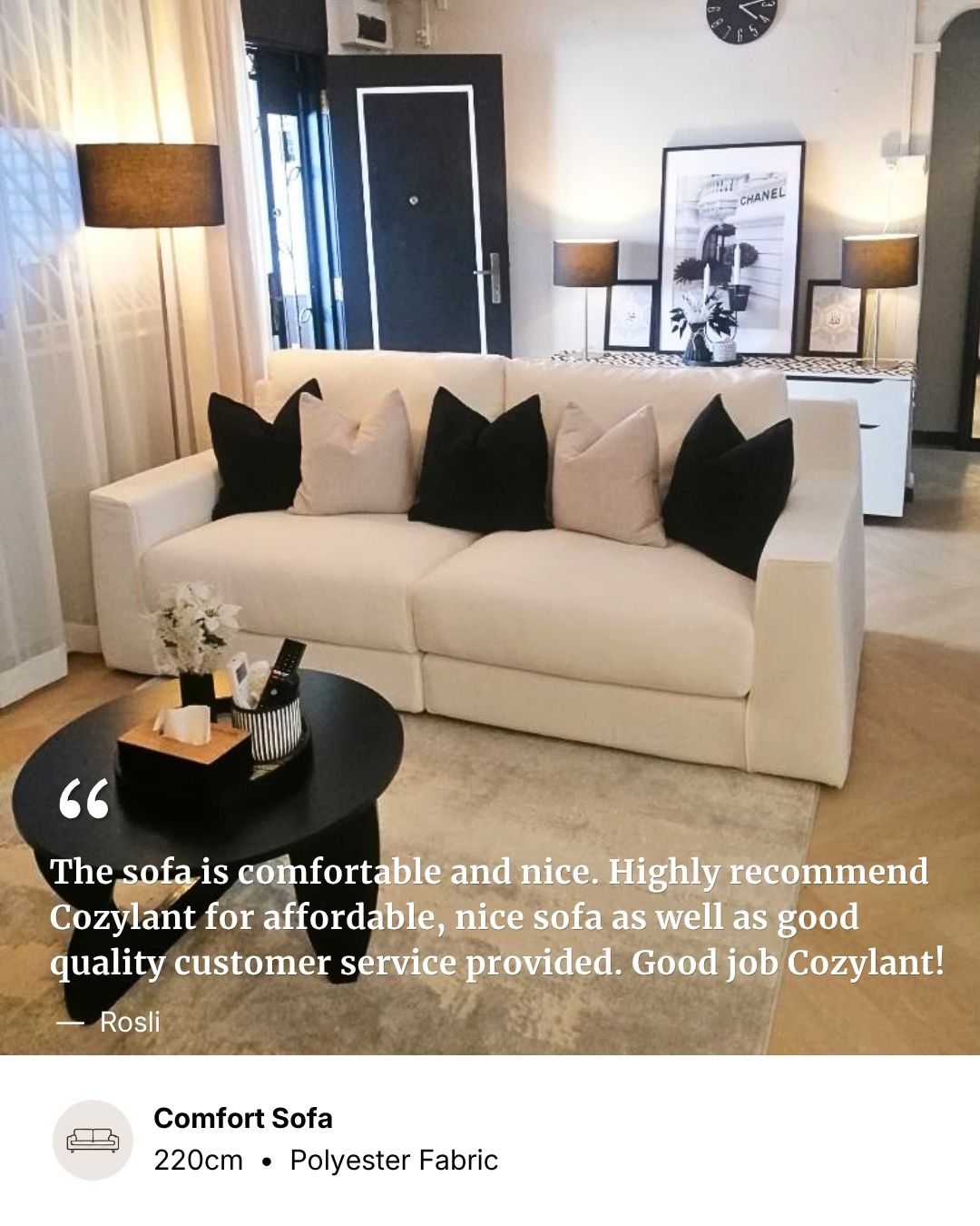 A cream-colored fabric sofa in a modern living room setting, styled with black and light beige throw pillows. A black coffee table and a round wall clock are in the foreground, with lamps and framed art in the background.