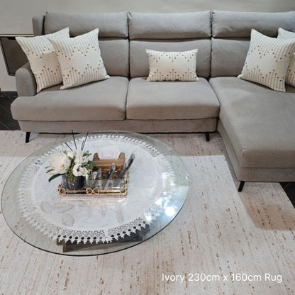 Gray sectional sofa with decorative pillows and a glass coffee table on an ivory rug.