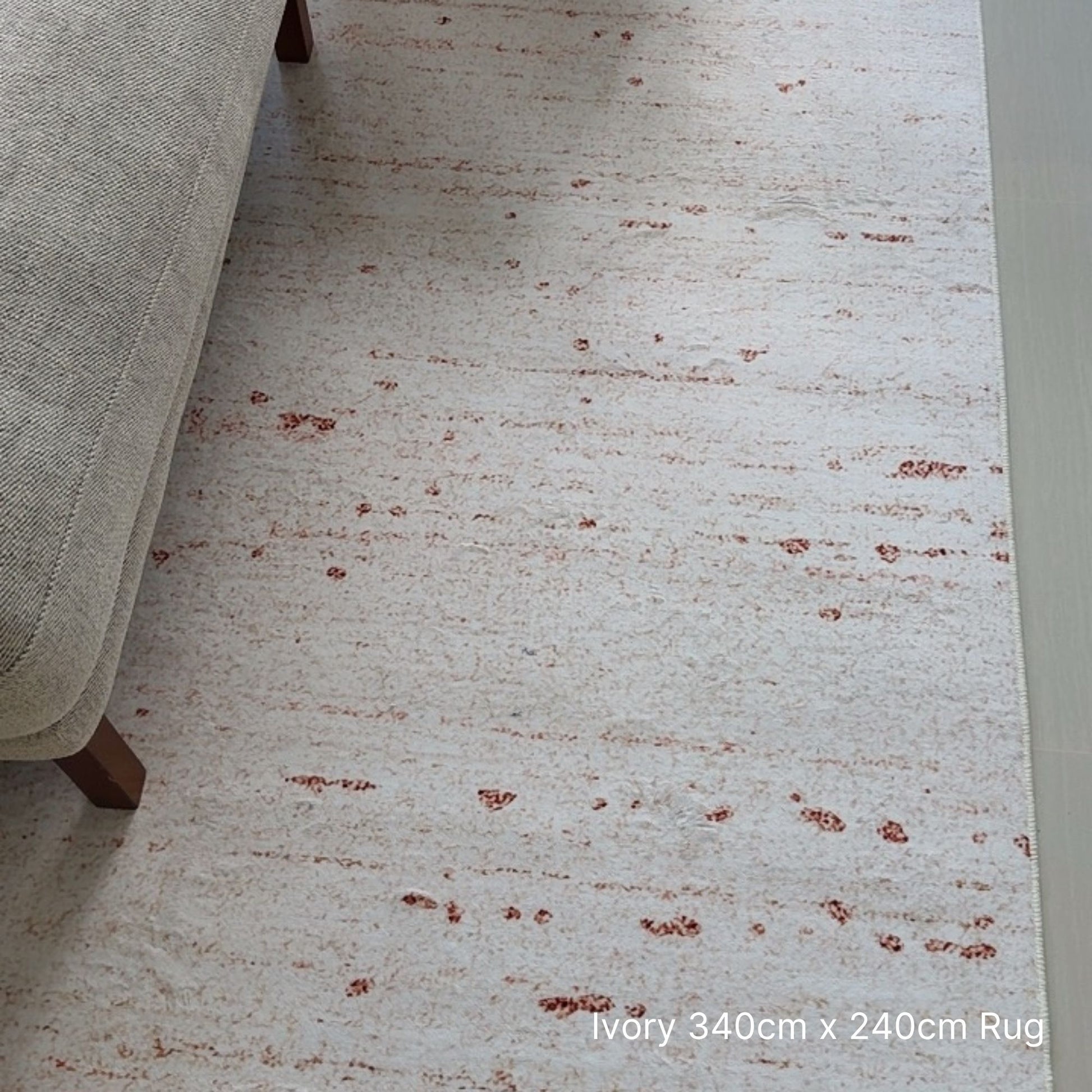 Ivory rug with brown speckles on a light-colored floor next to a beige sofa.