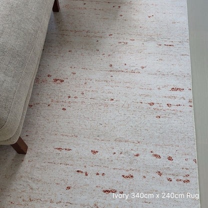 Ivory rug with brown speckles on a light-colored floor next to a beige sofa.
