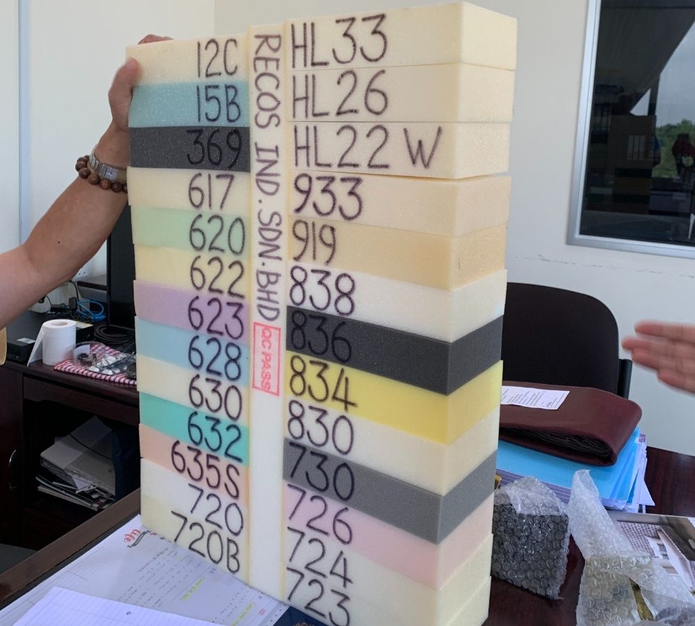 A hand holds a tall stack of colored foam blocks with printed color codes and a red vertical label reading 'RECOS IND. SAN BHP' in an office setting.