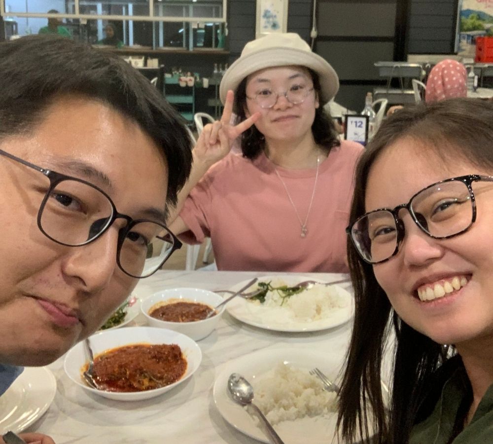 Three people posing together at a restaurant table with plates of food, including rice and red curry.