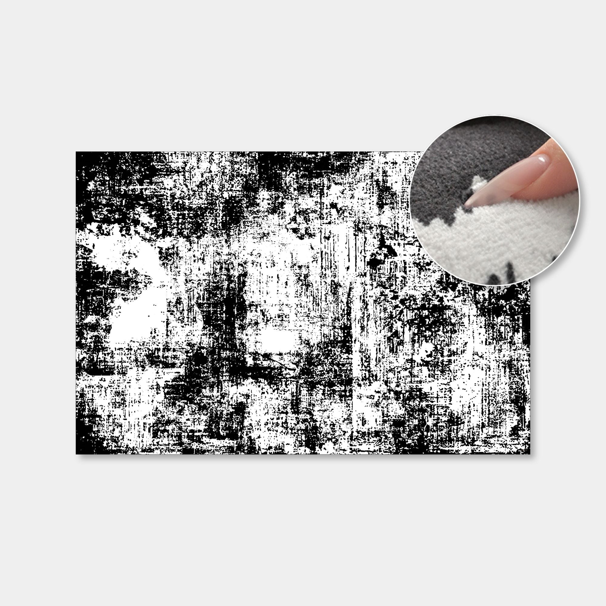 A rectangular black and white distressed grunge pattern sample shown on a light gray background, with a circular inset demonstrating a finger pressing into the textured surface.