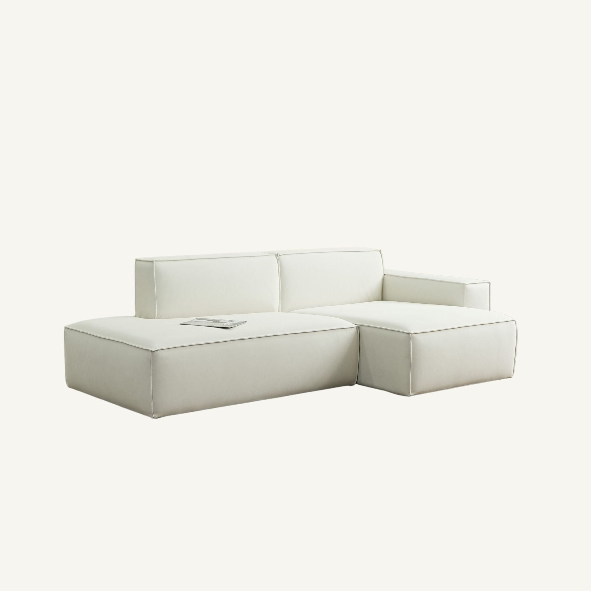 A modern modular sectional sofa in a light cream or off-white leather, featuring a left-facing chaise lounge and a right-facing armrest section, shown against a solid off-white background.