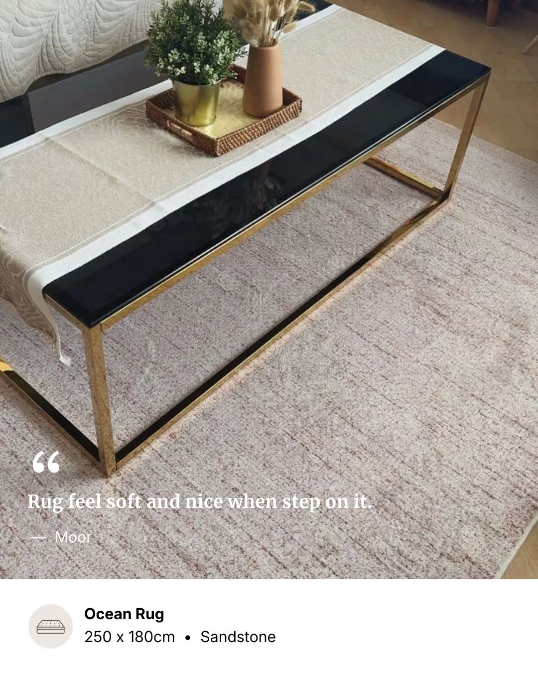 A close-up of a textured sandstone coffee table with a black top and gold metal frame, placed on a light beige rug. A white runner with a small potted plant sits on the table.