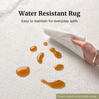 A close-up of a white textured rug with several amber water droplets on the surface. A hand is shown wiping away the water droplets with a cloth to show its water resistant properties