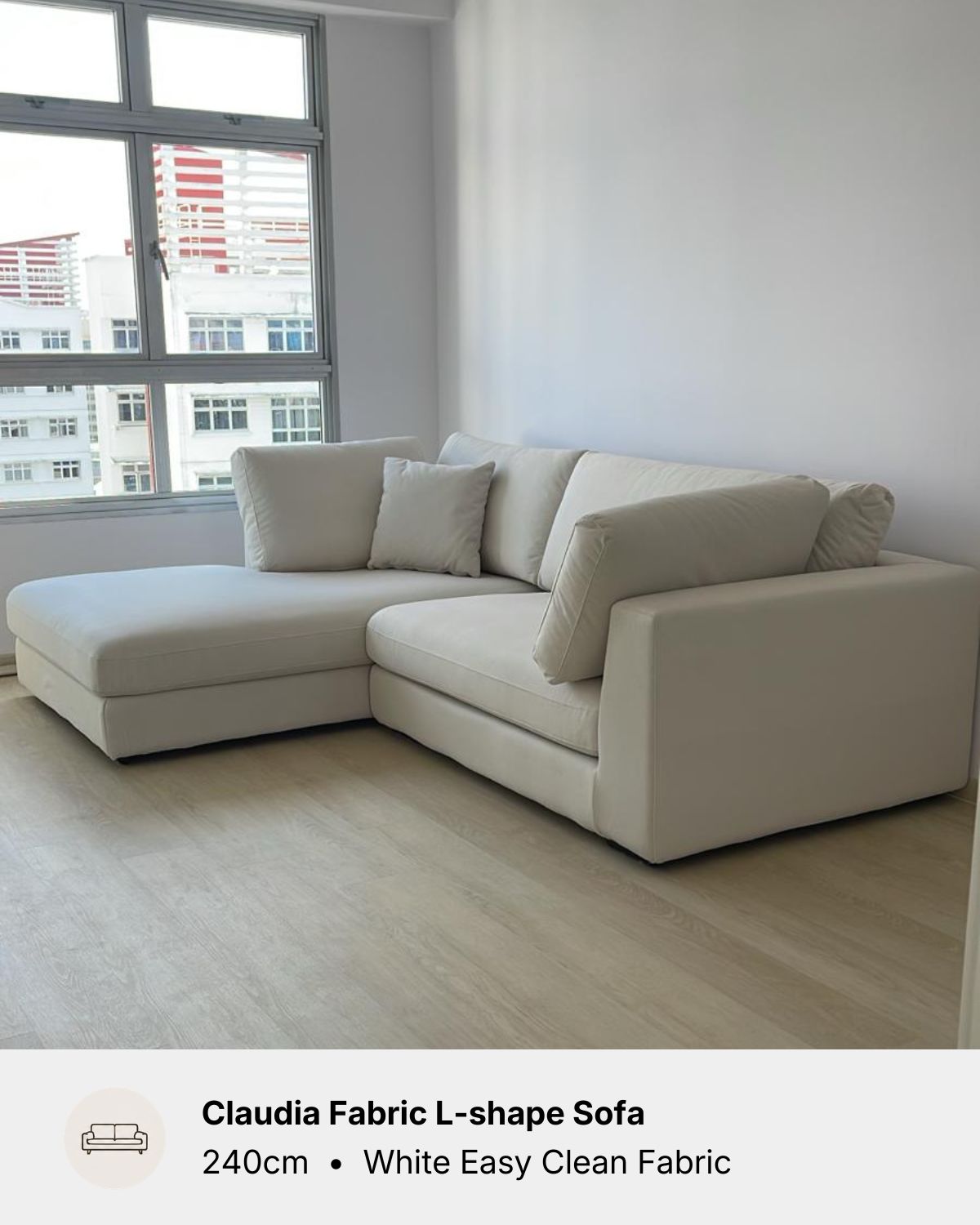 An L-shaped sectional sofa upholstered in white easy clean fabric, shown in a modern room with light wood floors and a large window. A text banner at the bottom reads 'Claudia Fabric L-shape Sofa 240cm • White Easy Clean Fabric'.