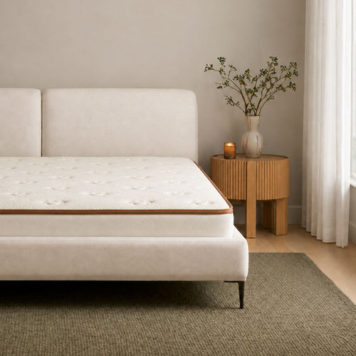 A modern upholstered bed frame with a tufted mattress, styled in a minimalist bedroom setting next to a wooden side table with a vase of branches.