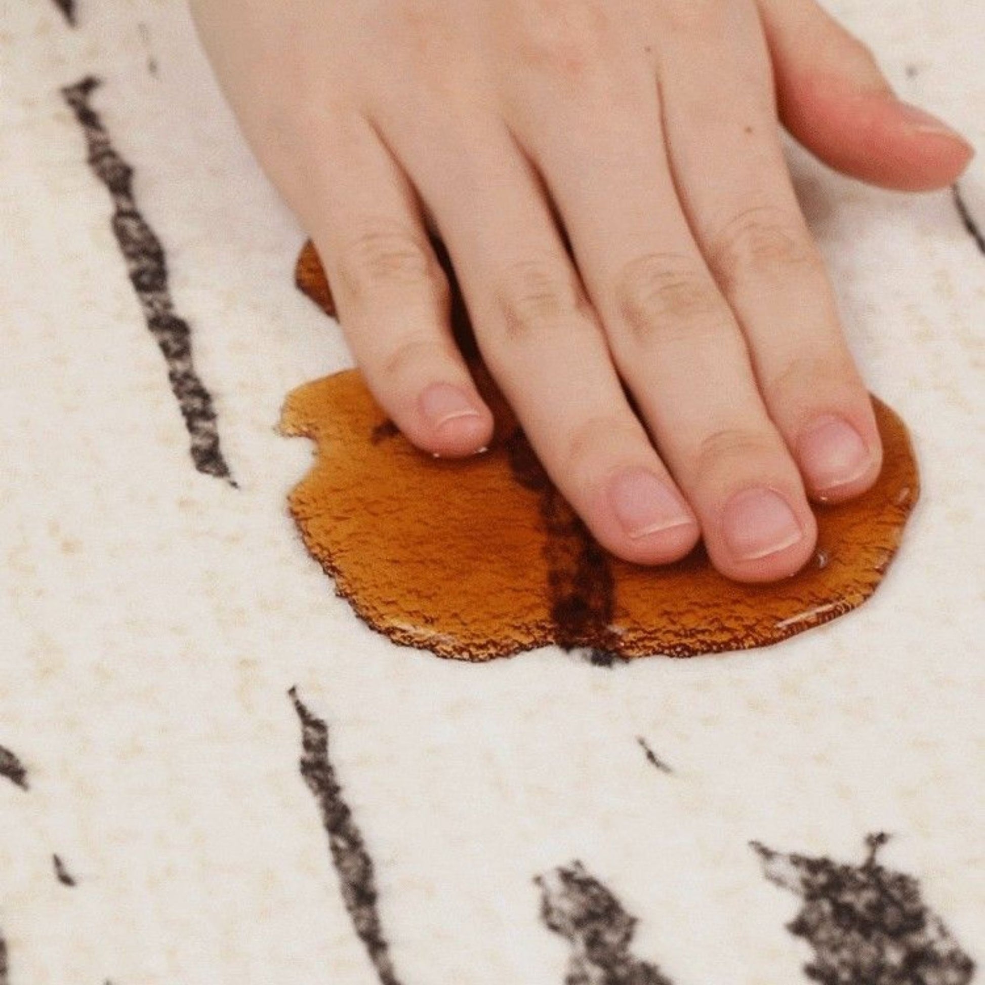 Hand pressing a brown liquid patch onto a textured rug surface