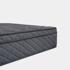 A close-up studio shot of a dark gray quilted mattress corner, showing the diamond-patterned fabric and stitched edge against a light gray background.