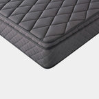 A close-up studio shot of a dark gray quilted mattress corner, showing the diamond-patterned top and textured side edge against a light gray background.