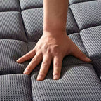 A close-up of a person's hand pressing down on a gray textured mattress to show its softness and tactile quality.