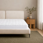 A modern upholstered bed frame with a tufted mattress, styled in a minimalist bedroom setting next to a wooden side table with a vase of branches.
