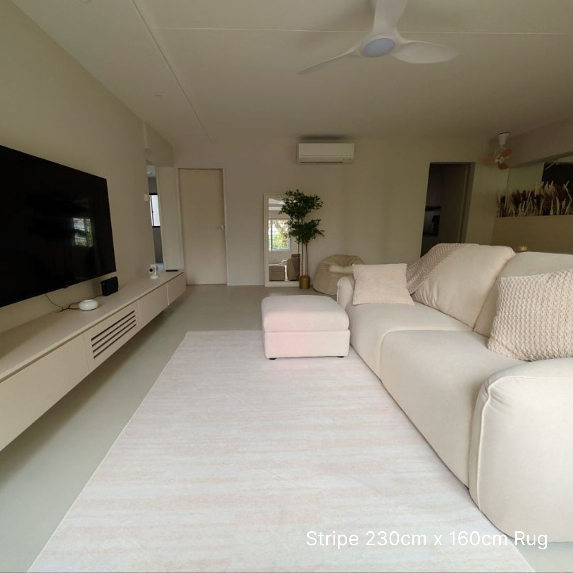 Modern living room with a large white rug, beige sofa, and flat-screen TV.
