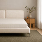 A modern platform bed with a textured cream upholstered frame and mattress, styled in a minimalist bedroom setting with a wooden side table, vase, and curtain.