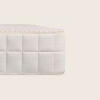 A close-up of a white quilted mattress corner with a textured top surface, set against a solid light beige background.