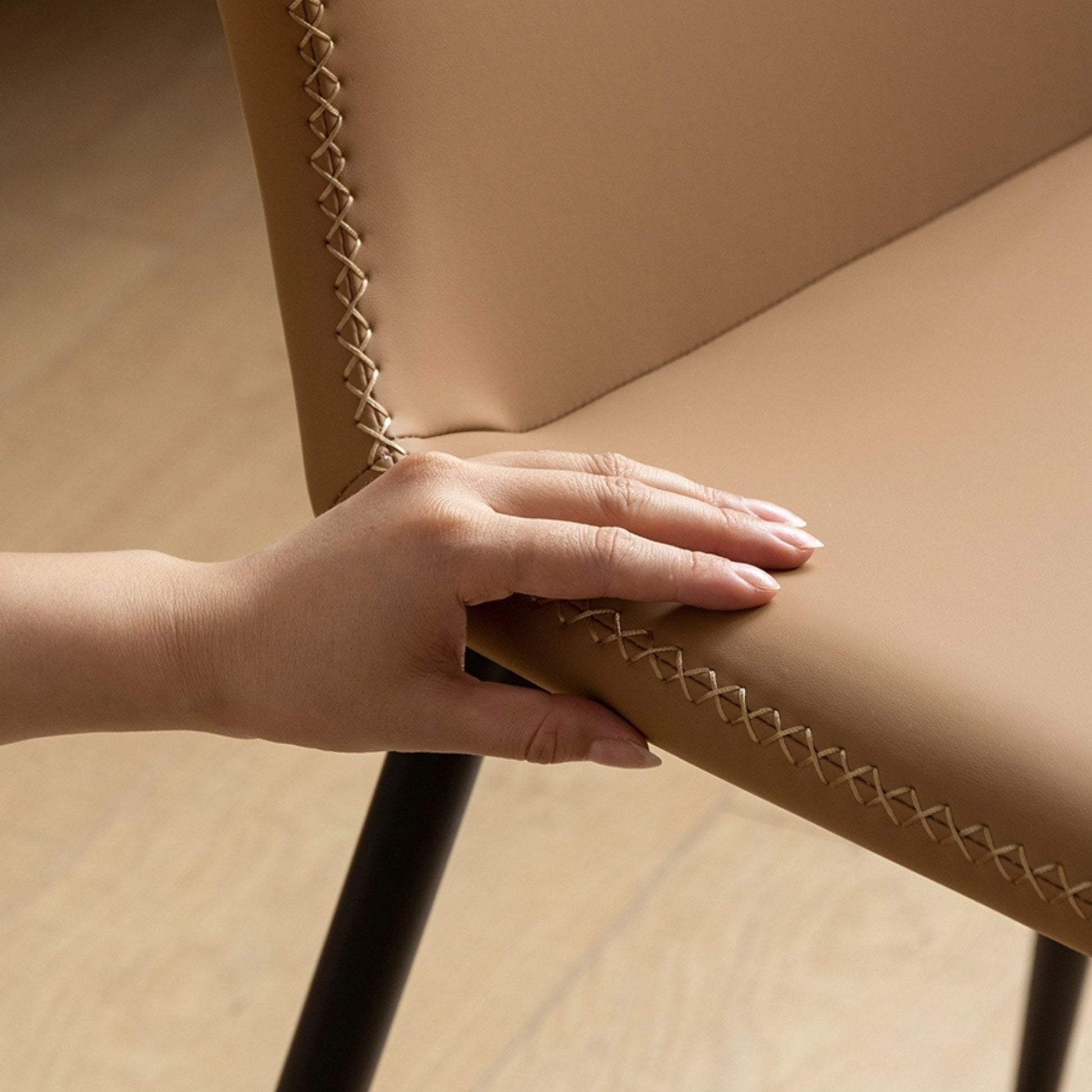 Hand touching a brown upholstered chair with braided trim
