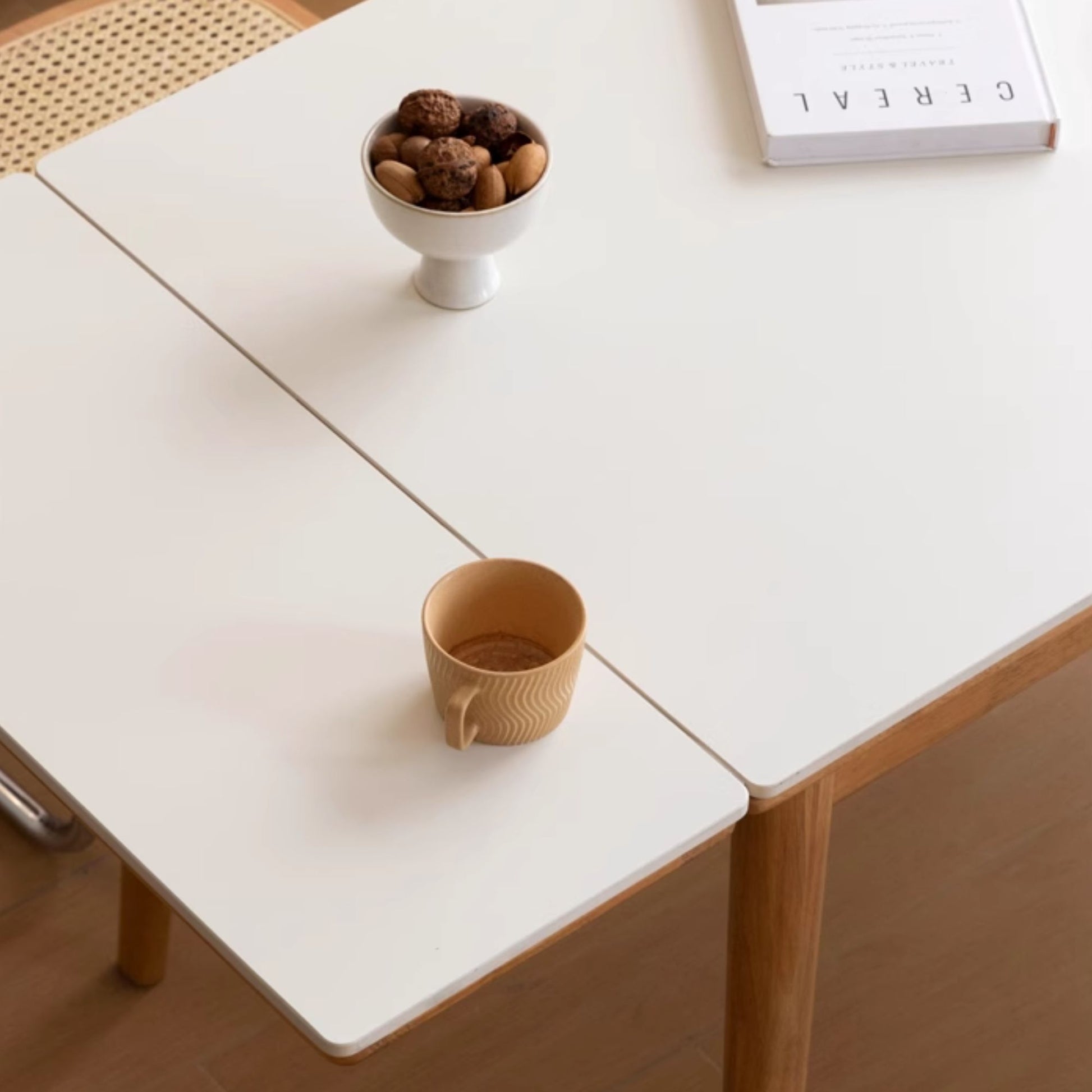 White table with a wooden cup and small bowl of nuts on a wooden floor.