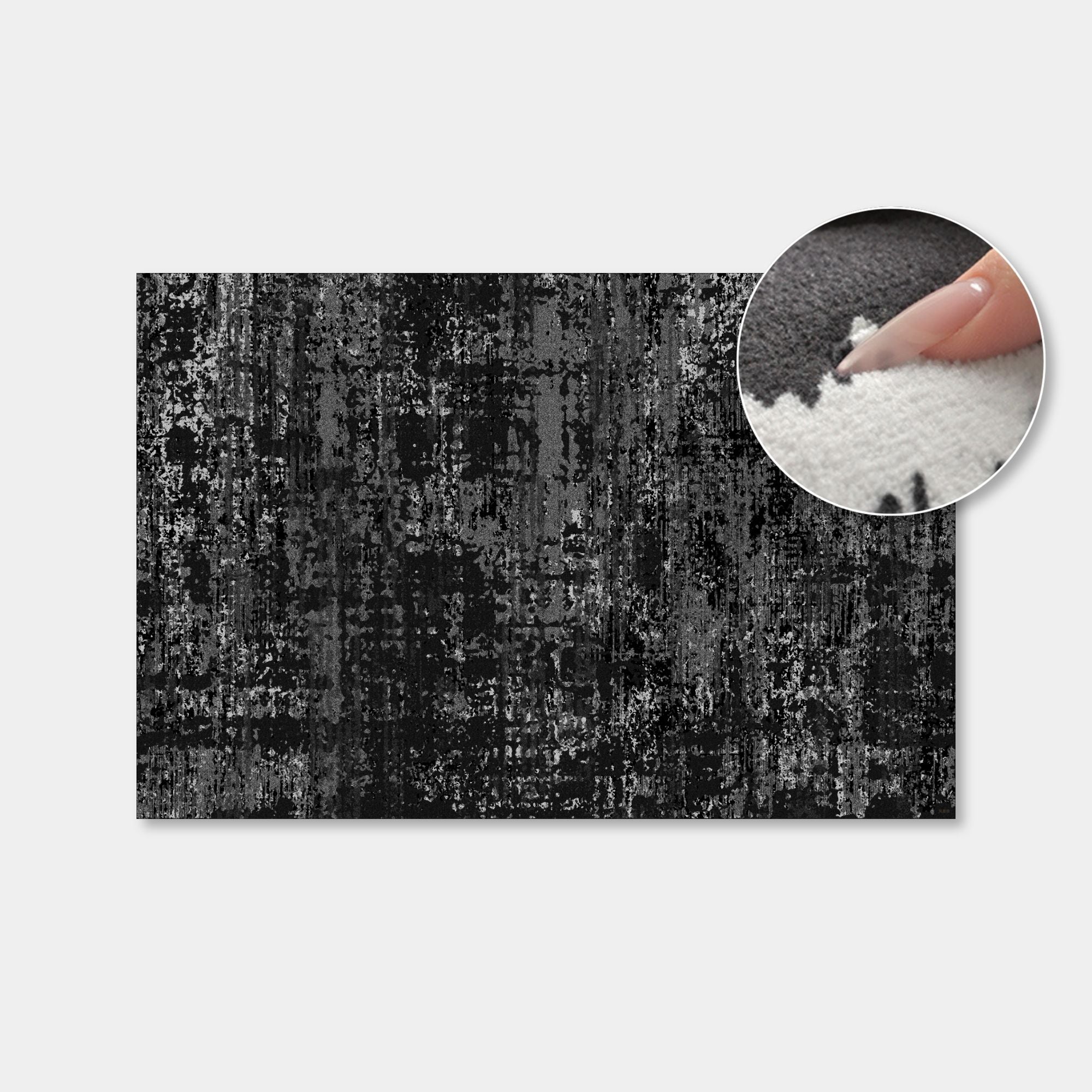 A rectangular black and gray distressed rug or mat shown on a light gray background, with a circular inset close-up of a finger pressing into the textured surface to demonstrate its plush, soft pile.
